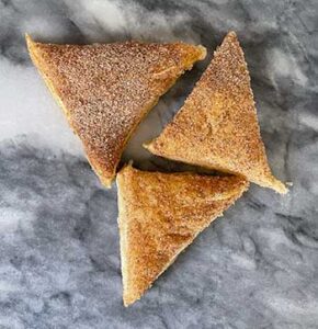 Three triangular pastries coated with sugar on a marble surface.