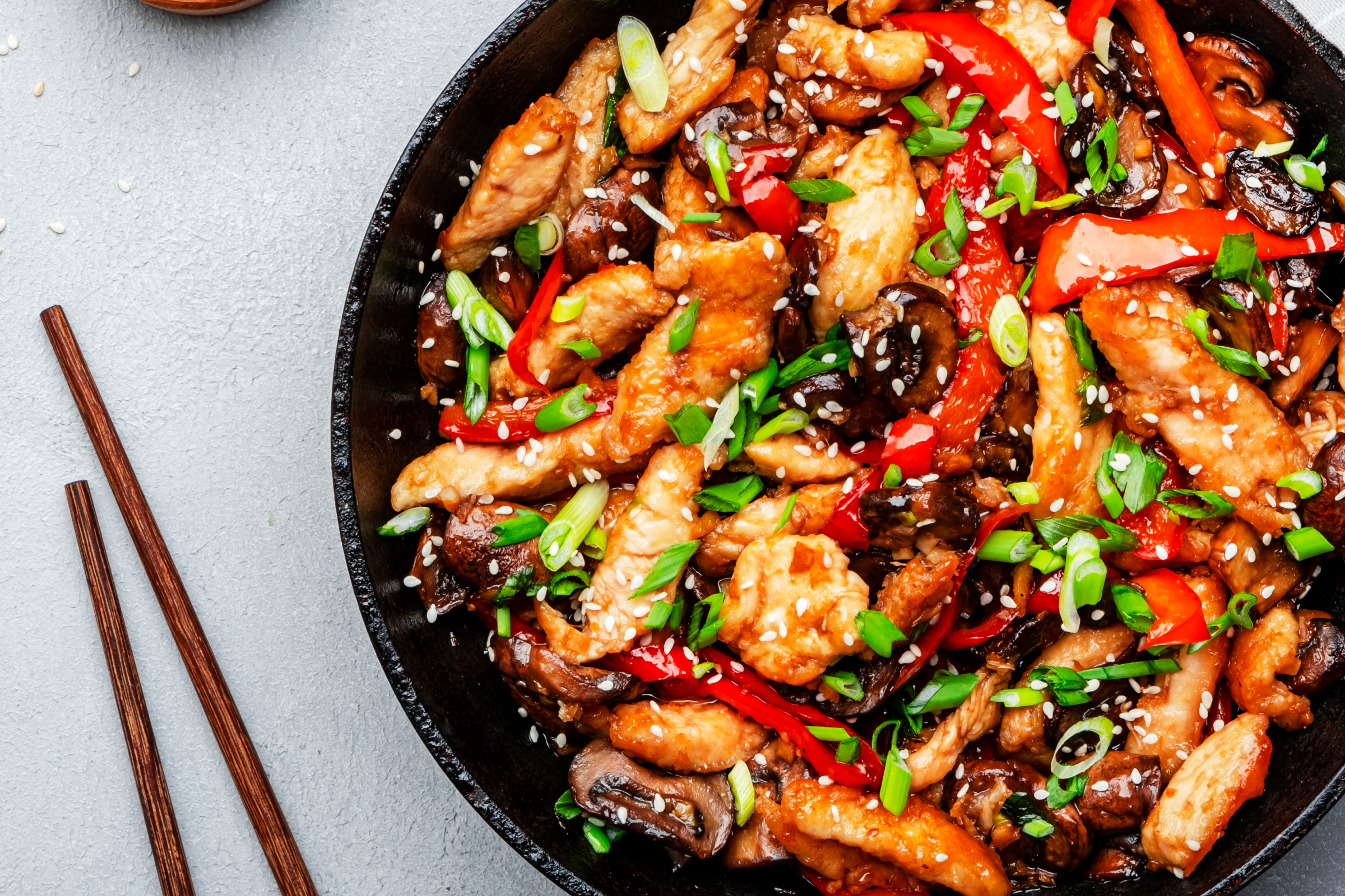 A vibrant stir-fry with chicken, red peppers, mushrooms, and green onions.