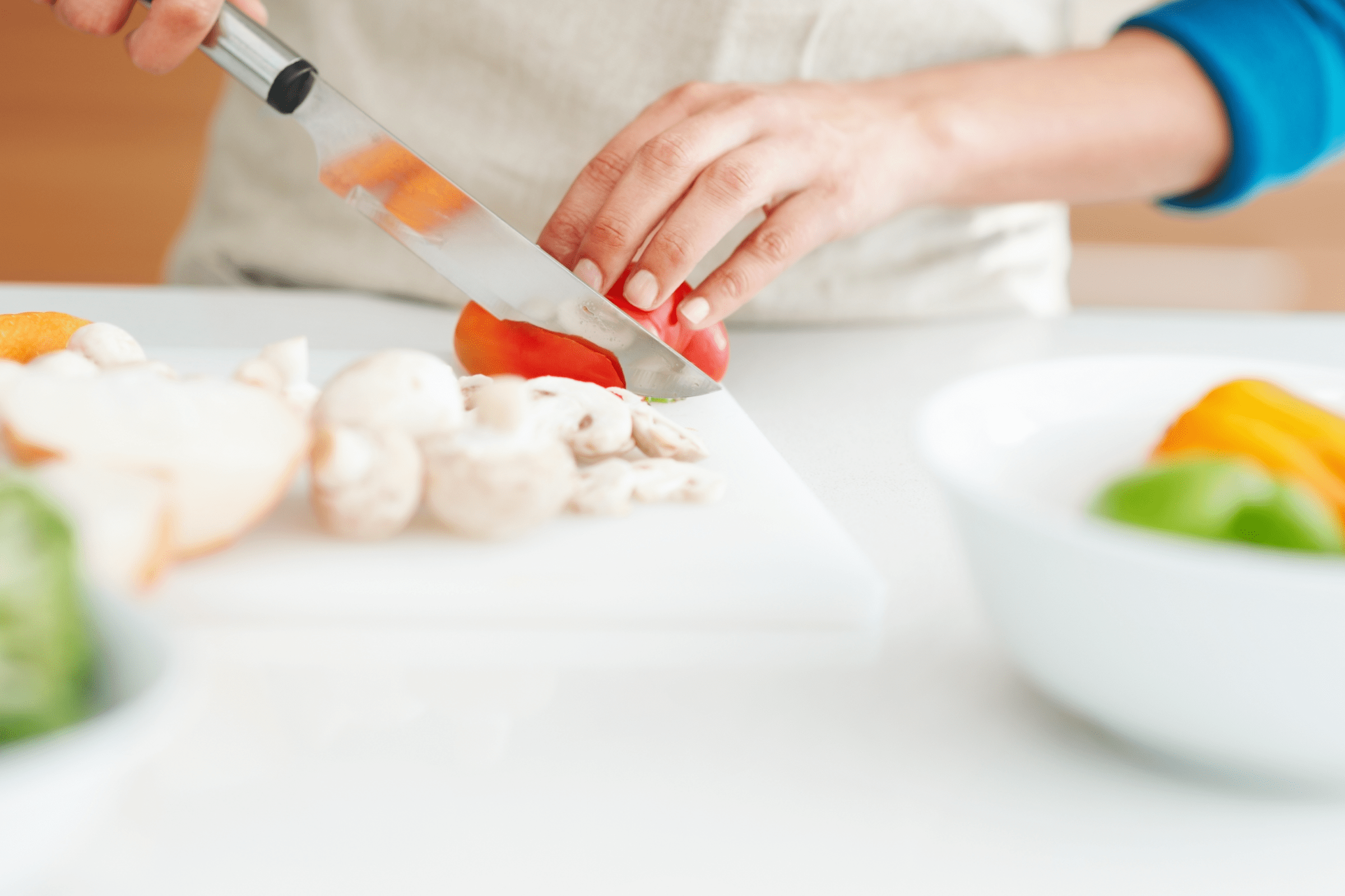 Person slicing red bell pepper on a white cutting board.