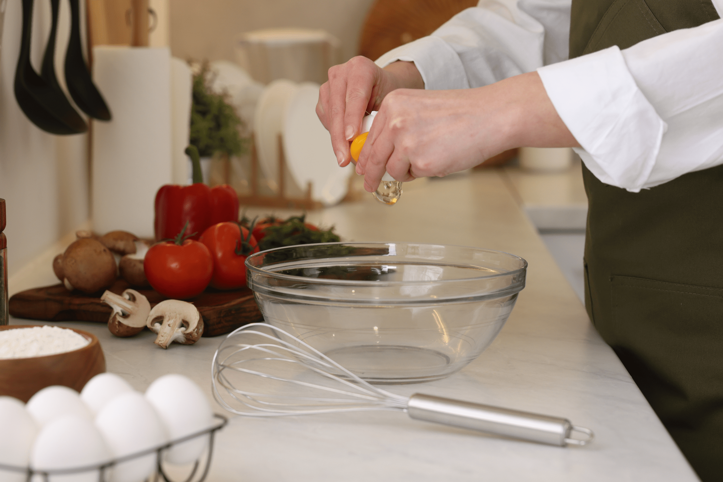 Person cracking an egg into a glass bowl in a kitchen.