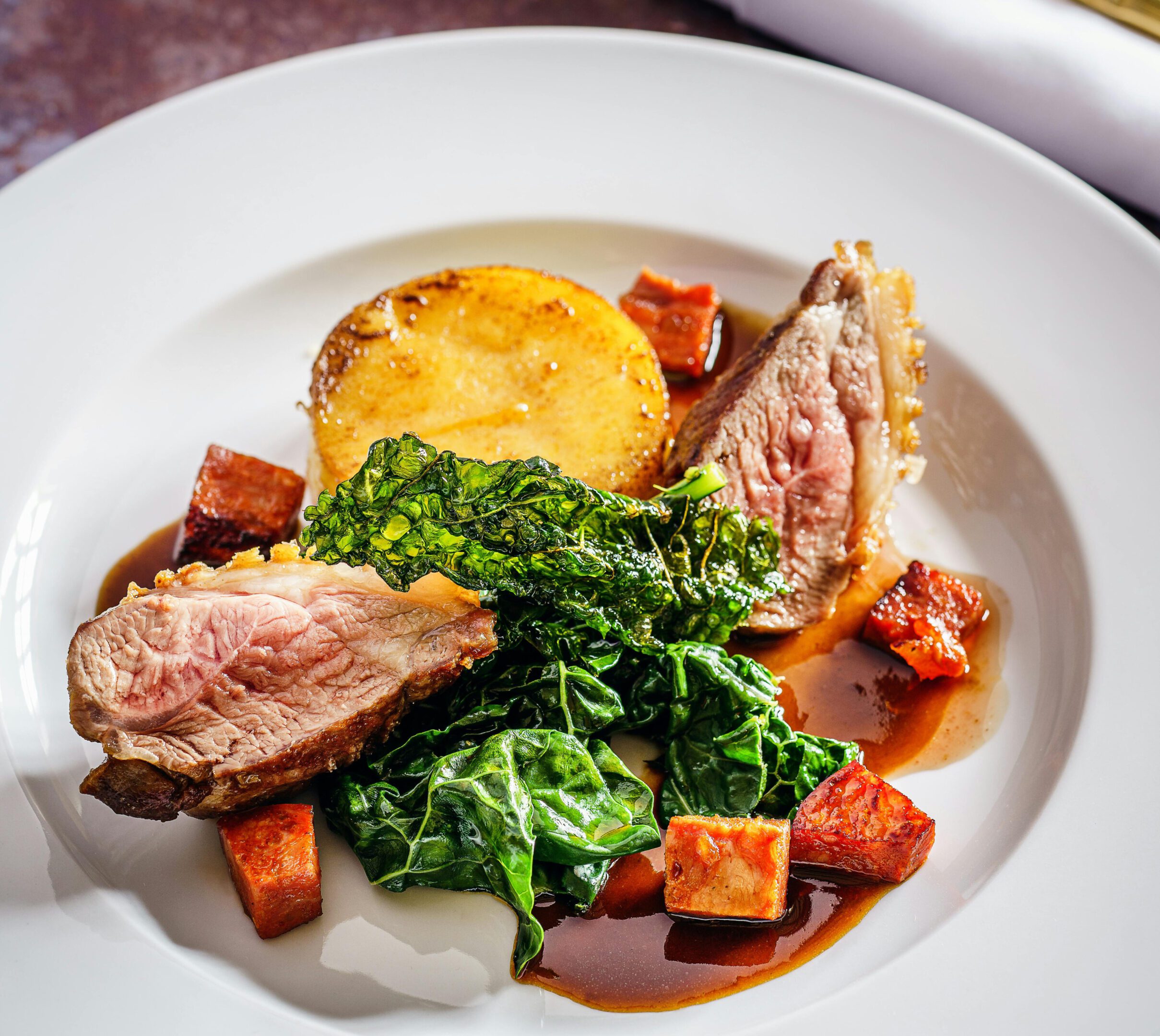 A gourmet dish with lamb chops, greens, roasted potatoes, and cubed sweet potatoes.