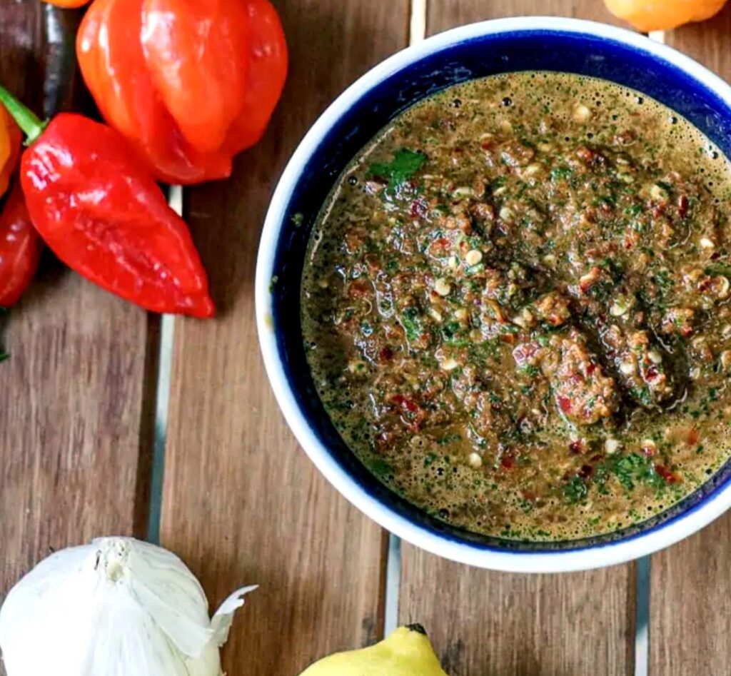 Bowl of spicy green sauce with peppers and garlic on wooden table.