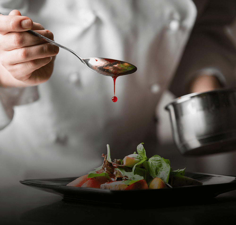 Chef drizzling sauce over a plated dish with precision.