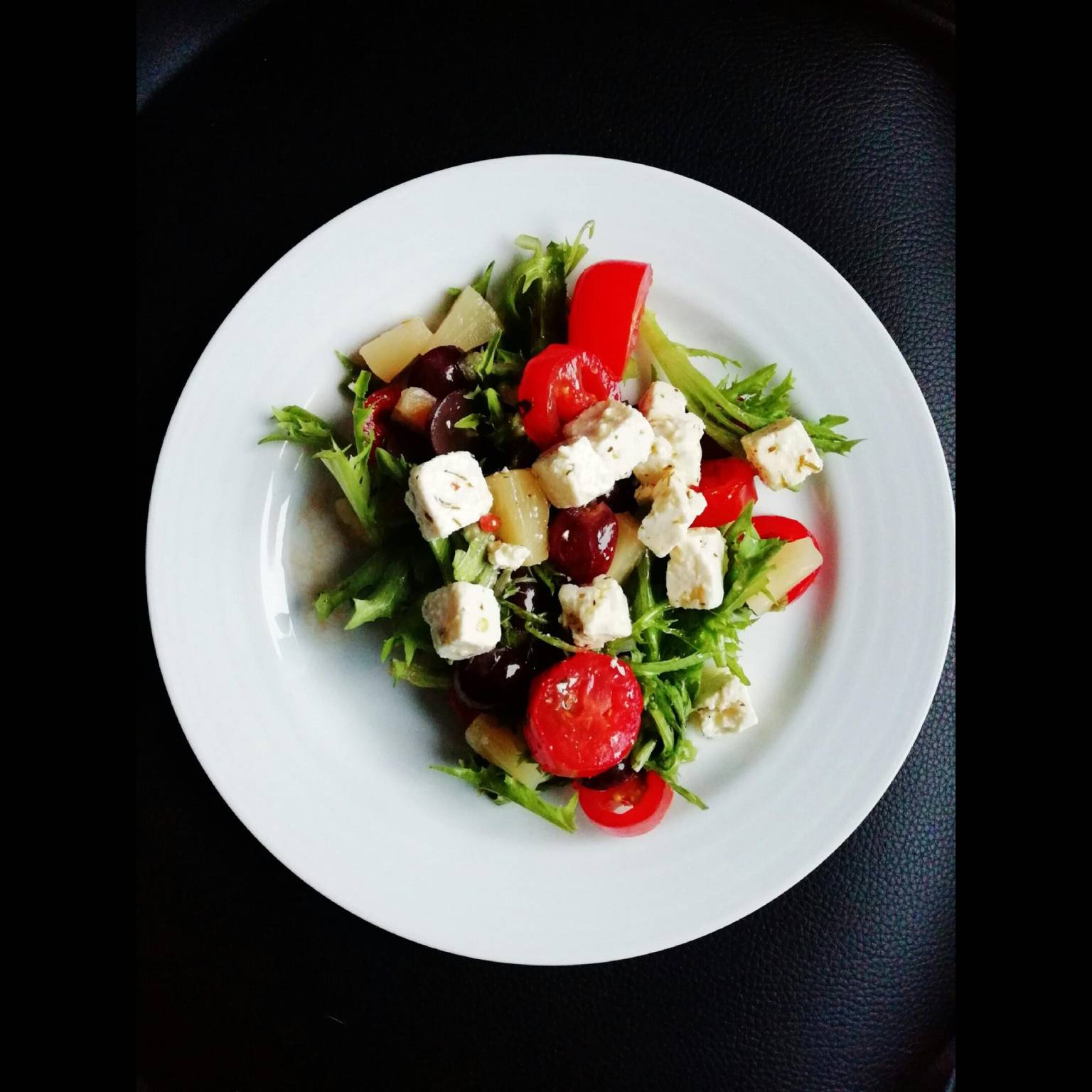 Fresh salad with tomatoes, lettuce, olives, and cheese on a white plate.