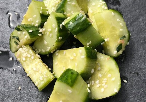 Chopped cucumber pieces sprinkled with sesame seeds on a dark surface.